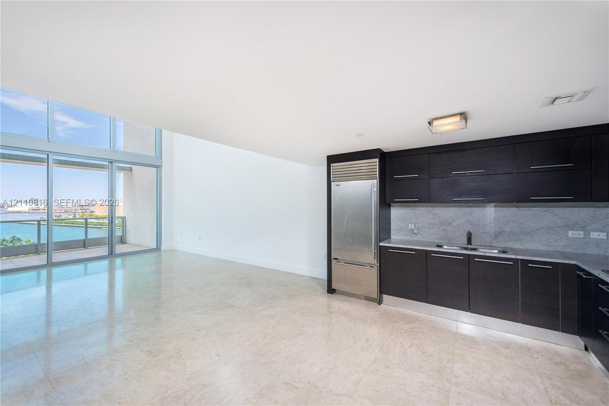 Kitchen featuring dark cabinetry, integrated stainless steel refrigerator, stone-style backsplash, and light-toned flooring, with floor-to-ceiling win