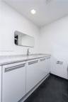 Custom white cabinetry with sleek horizontal pulls, stone-composite countertop, undermount sink, wall-mounted mirror with rounded edges, and dark tile