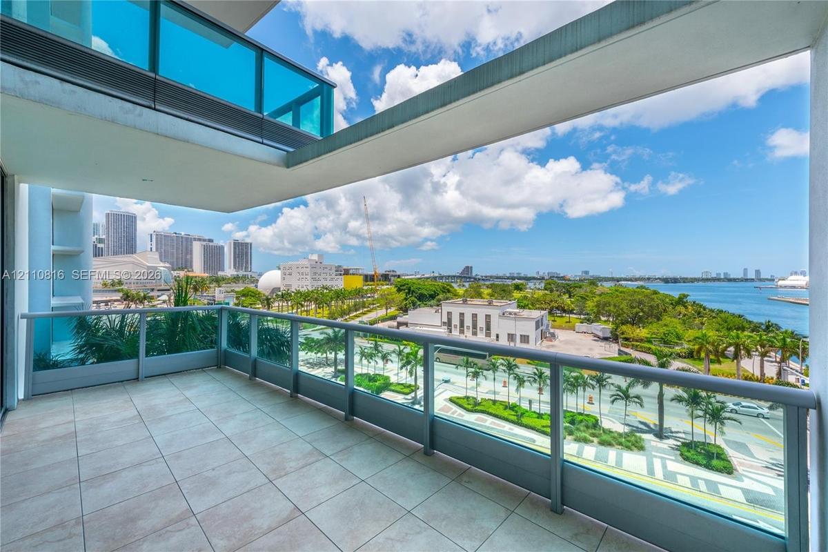 Private balcony with ceramic tile flooring and glass panel railings overlooking a waterfront cityscape