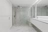 Bathroom featuring floor-to-ceiling veined stone-finish tile, glass-enclosed shower with built-in bench, floating dual-sink vanity, and expansive wall