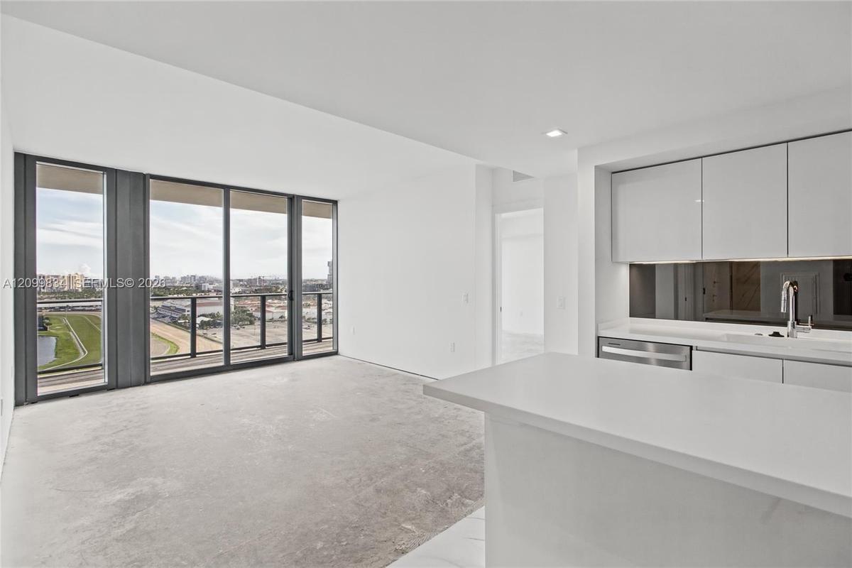 Kitchen featuring high-gloss cabinetry, white solid-surface countertops, and a dark mirrored backsplash, complemented by expansive floor-to-ceiling wi