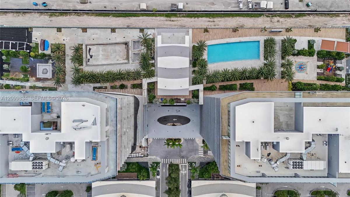 Aerial perspective featuring a central swimming pool, landscaped palm tree courtyards, paved pedestrian walkways, and structured surface parking