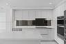 Kitchen featuring high-gloss white cabinetry, white stone countertops, a dark mirrored backsplash, integrated double wall ovens, and recessed lighting