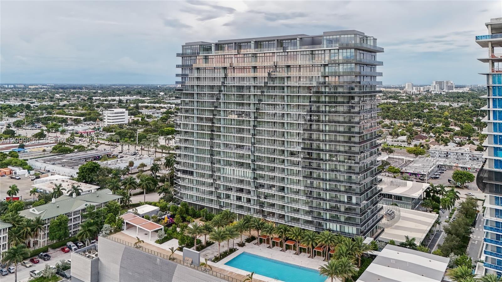 High-rise residential building featuring floor-to-ceiling glass windows, private balconies, a ground-level swimming pool, and dedicated cabana structu