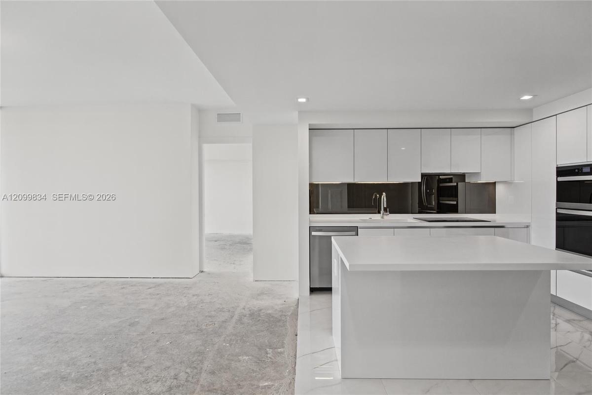 Contemporary kitchen featuring high-gloss white cabinetry, a waterfall-edge central island, integrated stainless steel appliances, a dark mirrored bac