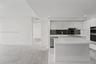 Contemporary kitchen featuring high-gloss white cabinetry, a waterfall-edge central island, integrated stainless steel appliances, a dark mirrored bac