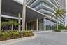 Covered porte-cochere entrance featuring floor-to-ceiling glass paneling, concrete structural columns, recessed exterior lighting, and manicured tropi