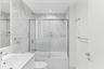 Bathroom featuring floor-to-ceiling stone-finish tile surround, a built-in bathtub with a chrome-framed sliding glass enclosure, a wall-mounted vanity