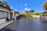 Exterior featuring a patterned paved driveway, covered front entryway with tiled flooring, stone-accented pillar, and perimeter privacy fencing