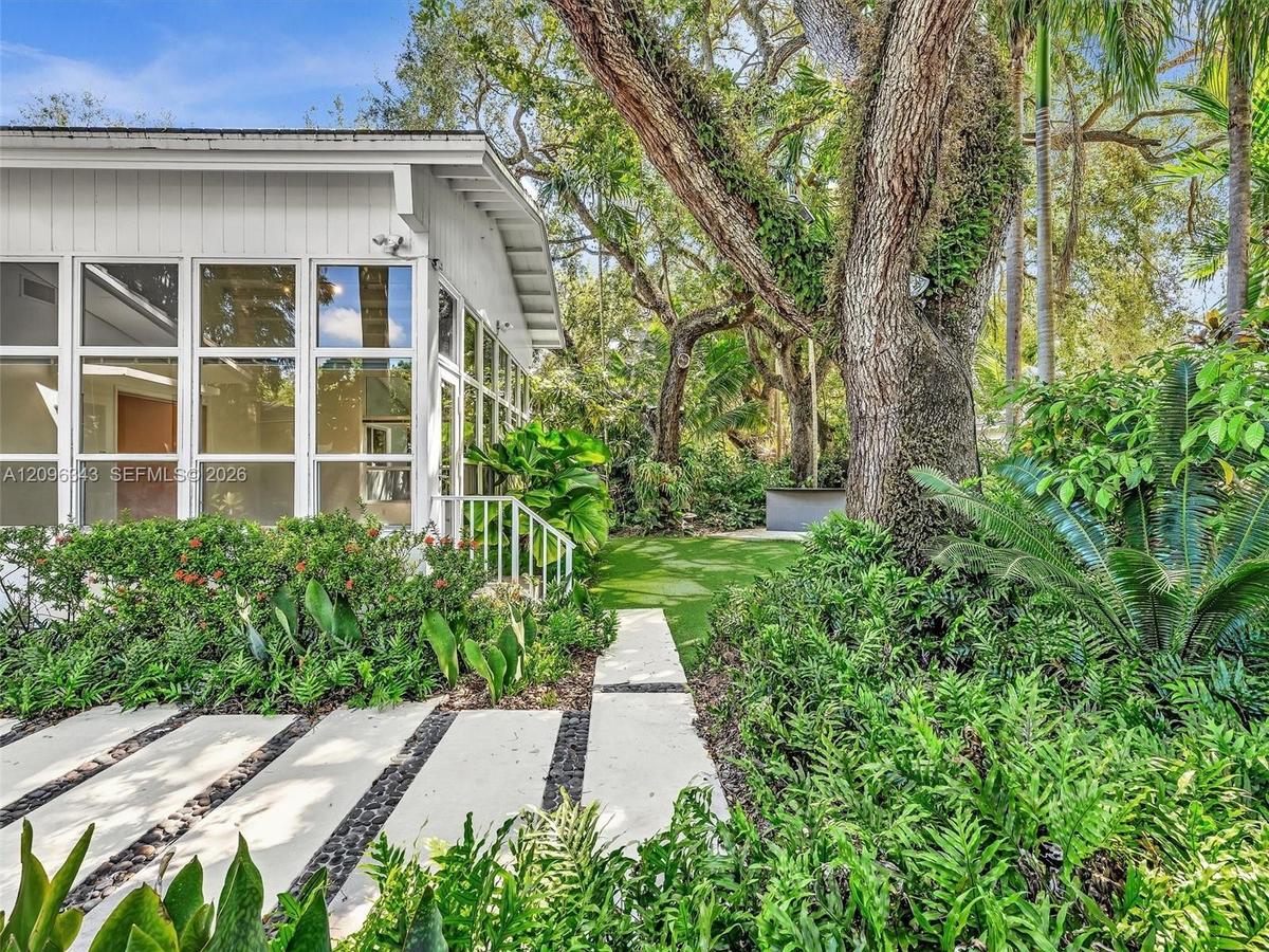 Bright sun room spills to landscaped yard with turf and concrete landing paths. House for rent in Coconut Grove.