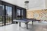 Modern recreation room featuring a regulation pool table, geometric wood-finish accent wall with multi-colored chevron detailing, floor-to-ceiling gla