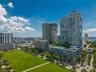High-rise condominium towers featuring glass-paneled balconies and a multi-level recreational deck with a swimming pool, situated beside a expansive l