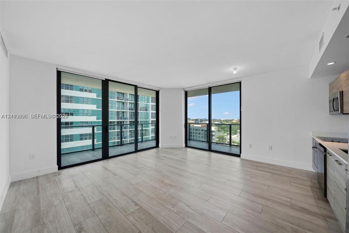 Floor-to-ceiling sliding glass doors, neutral wood-finish flooring, recessed lighting, and kitchen cabinetry featuring a contemporary wood-grain finis