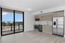 Kitchen featuring wood-finish cabinetry, stainless steel appliances, and quartz countertops, complemented by wood-finish flooring and floor-to-ceiling
