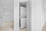 Laundry closet featuring a white stacked washer and dryer unit enclosed by bi-fold louvered doors, situated over light-toned wood-finish flooring