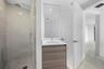 Glass-enclosed shower with rainfall showerhead, wood-finish vanity with countertop basin, and large-format tile flooring