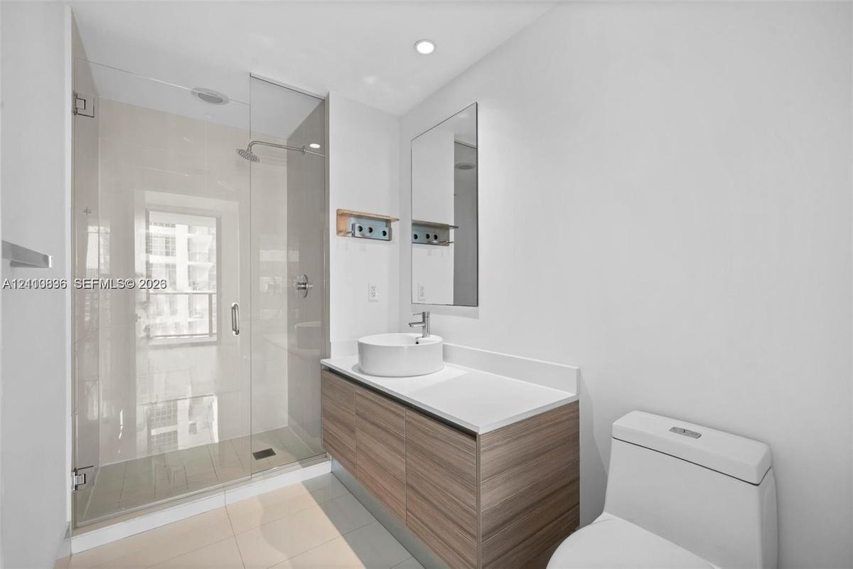 Bathroom featuring a wood-finish floating vanity, circular vessel sink, white solid-surface countertop, and a walk-in glass-enclosed shower with polis