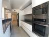 Kitchen featuring white flat-panel cabinetry, charcoal solid-surface countertops, stainless steel built-in double oven and microwave, recessed lightin