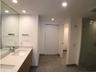 Floating wood-finish double vanity with stone countertop, recessed lighting, expansive wall-to-wall mirror, and glass-enclosed shower with tiled floor