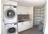 Utility area featuring white flat-panel cabinetry, a solid-surface countertop, an integrated sink with a chrome faucet, a stacked washer and dryer uni