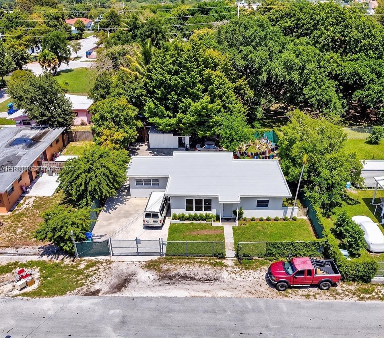Single-story residence featuring a metal roof, concrete driveway, fenced perimeter, and mature landscaping