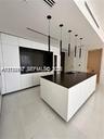Modern kitchen featuring white flat-panel cabinetry, a central island with a dark countertop, recessed lighting, and a series of minimalist pendant li