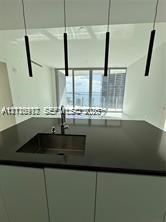 Modern kitchen island featuring a solid-surface countertop, integrated stainless steel undermount sink, gooseneck faucet, and four cylindrical pendant