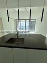 Modern kitchen island featuring a solid-surface countertop, integrated stainless steel undermount sink, gooseneck faucet, and four cylindrical pendant