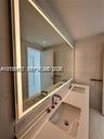 Dual-sink vanity featuring a solid surface countertop, undermount basins, polished chrome fixtures, and a large, full-width LED-backlit mirror