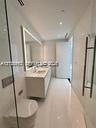 Modern bathroom featuring floor-to-ceiling tile, a floating dual-sink vanity with integrated lighting, a wall-mounted toilet, and a glass-enclosed sho