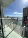 Private balcony featuring glass railings and tile flooring, overlooking urban skyline and coastal water