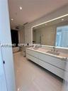 Floating dual-sink vanity with matte finishes, quartz countertop, large backlit mirror, and freestanding soaking tub