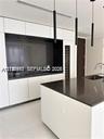 Modern kitchen featuring white flat-panel cabinetry, dark stone countertops, a built-in wine refrigerator, and cylindrical pendant lighting