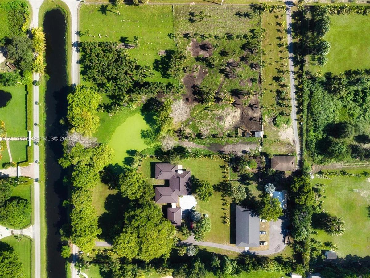 Aerial perspective of a sprawling property featuring extensive acreage, mature landscaping, a private water feature, an attached garage, and a dedicat
