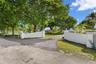Gated entry featuring stucco-finished masonry pillars, a paved driveway, and mature canopy trees