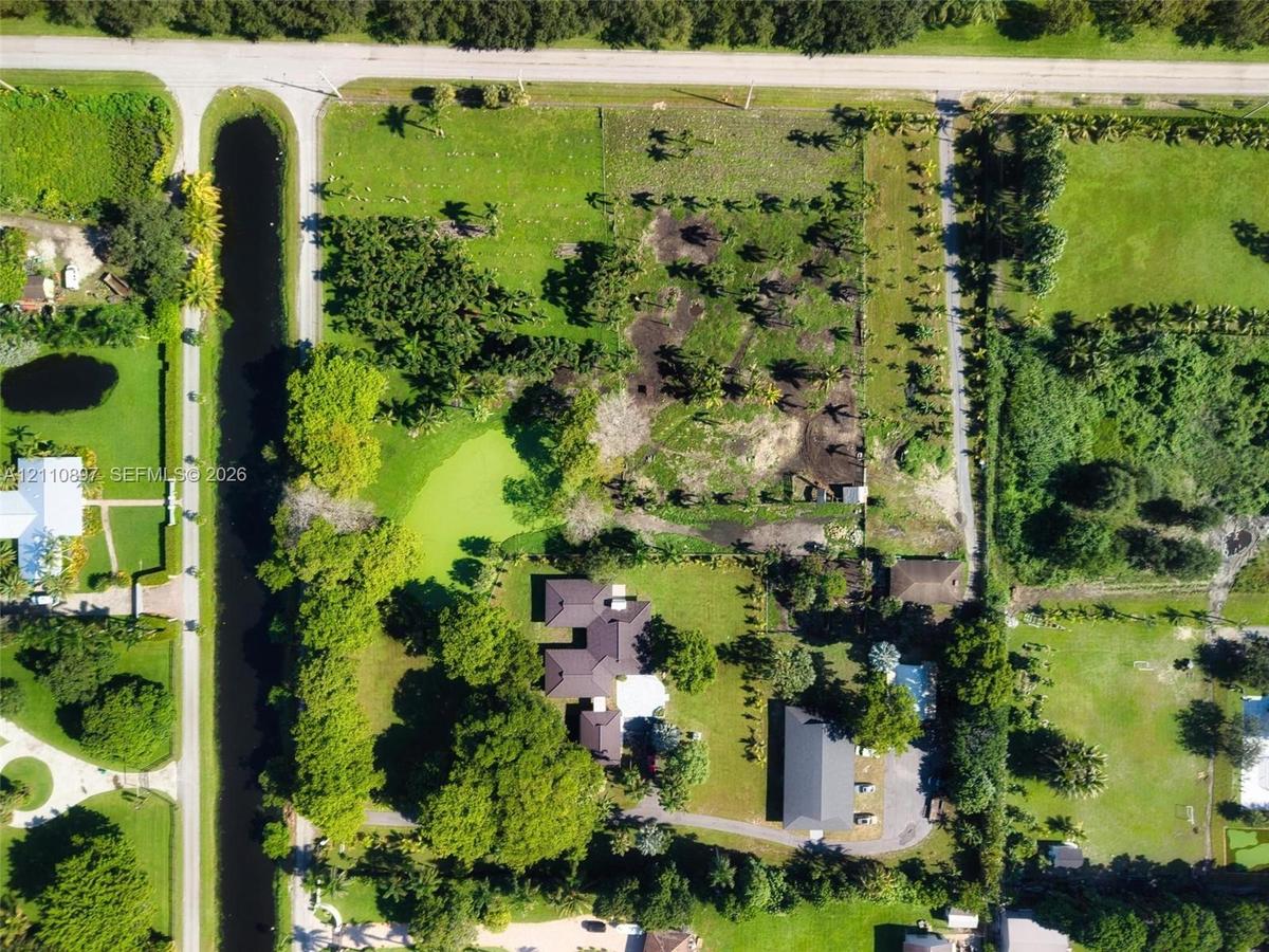 Aerial perspective of a sprawling lot featuring a multi-wing residence, a secondary detached structure, mature perimeter landscaping, and a natural wa