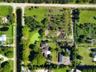 Aerial perspective of a sprawling lot featuring a multi-wing residence, a secondary detached structure, mature perimeter landscaping, and a natural wa