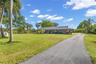 Single-story residence featuring a covered front porch, asphalt driveway, and expansive lawn with mature palm trees