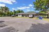 Single-story residence featuring an expansive asphalt parking area, a covered porch, and mature palm trees