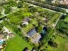 Aerial perspective of a sprawling property featuring extensive open green space, mature canopy trees, asphalt driveways, and multiple residential stru