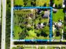Aerial view of a sprawling rectangular lot featuring expansive grassy acreage, mature trees, a private pond, and multiple structures