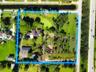 Aerial view of expansive lot featuring a multi-structure property, mature trees, a central pond, and paved driveway access