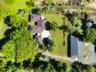 Aerial perspective of a sprawling property featuring mature canopy trees, a dedicated secondary structure with a dark shingle roof, paved driveway, an
