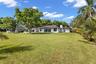 Single-story residence featuring a hipped tile roof, white stucco exterior, expansive lawn, mature specimen trees, and palm landscaping