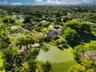 Aerial perspective of a sprawling property featuring a multi-wing residence, a private pond, expansive green space, mature canopy trees, and palm vege