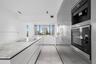 Contemporary kitchen featuring a stone-surface island with an integrated cooktop, flat-panel cabinetry, high-end built-in stainless steel appliances, 