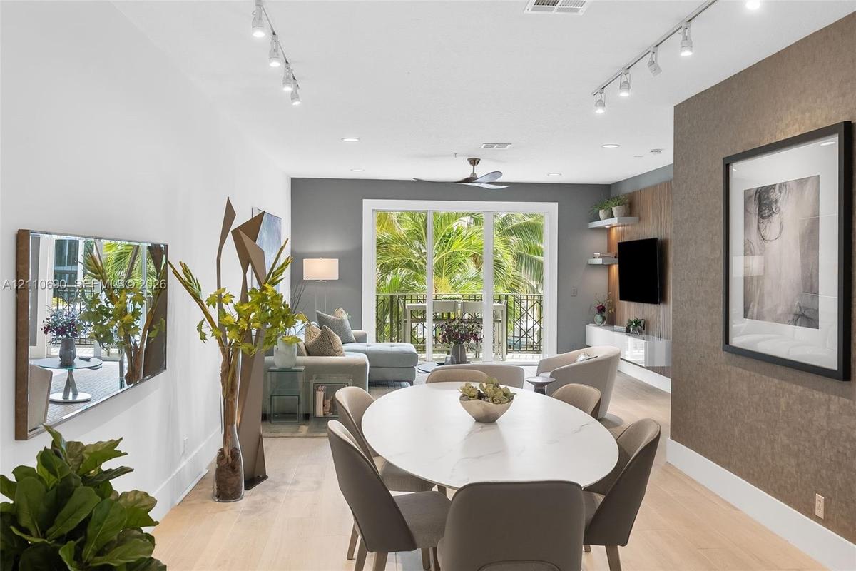 Living area featuring light-toned wood-finish flooring, adjustable track lighting, a textured accent wall, integrated floating shelving, and a glass-p