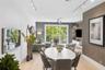 Living area featuring light-toned wood-finish flooring, adjustable track lighting, a textured accent wall, integrated floating shelving, and a glass-p