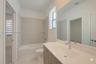 Bathroom featuring a wood-finish vanity with a white integrated sink, full-width wall mirror, and a tub-shower combination with floor-to-ceiling tile 