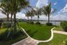 Backyard featuring artificial turf, paver walkways, mature palm trees, a perimeter metal fence, and water frontage